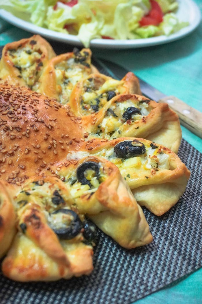 Freshly baked bread with olives and cheese, topped with sesame seeds, served with salad.
